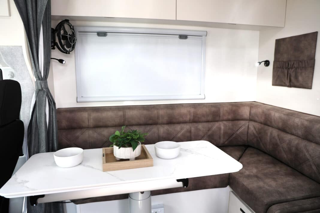 a large l-shape lounge within this JB Touring motorhome, provides room for two laptops for travellers to work comfortably side-by-side. Note the beautiful teak mottled chocolate coloured upholstery with lumbar support