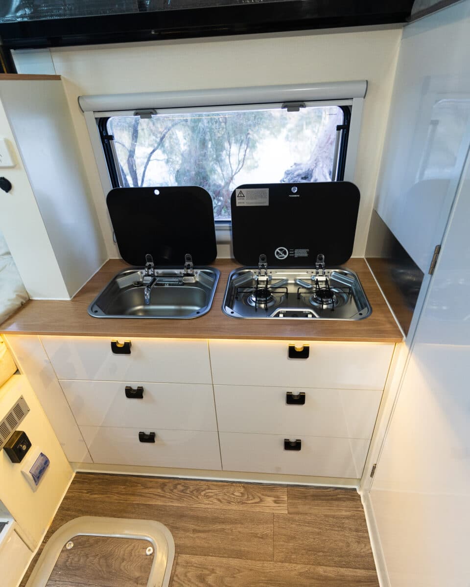 A galley kitchen in the Arctic Glacier 14TS featuring drawers and a three burner gas cooktop and a sink complements the outdoor kitchen