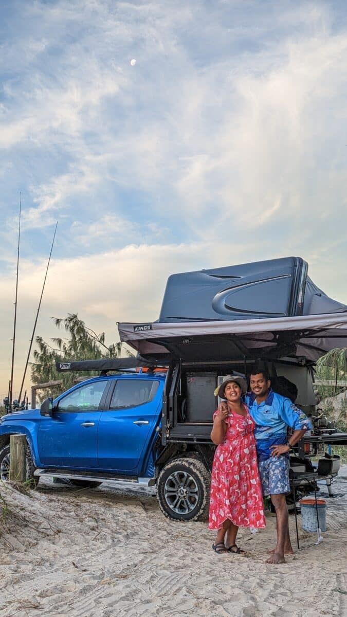 A couple stand in front of a 4WD with an open rooftop tent setup.