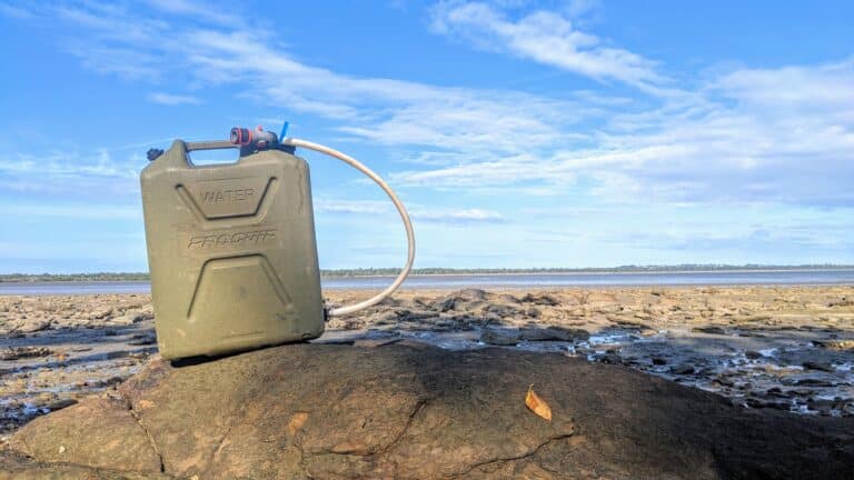 Modified water jerry can with control valve and hose fitting on a rock.
