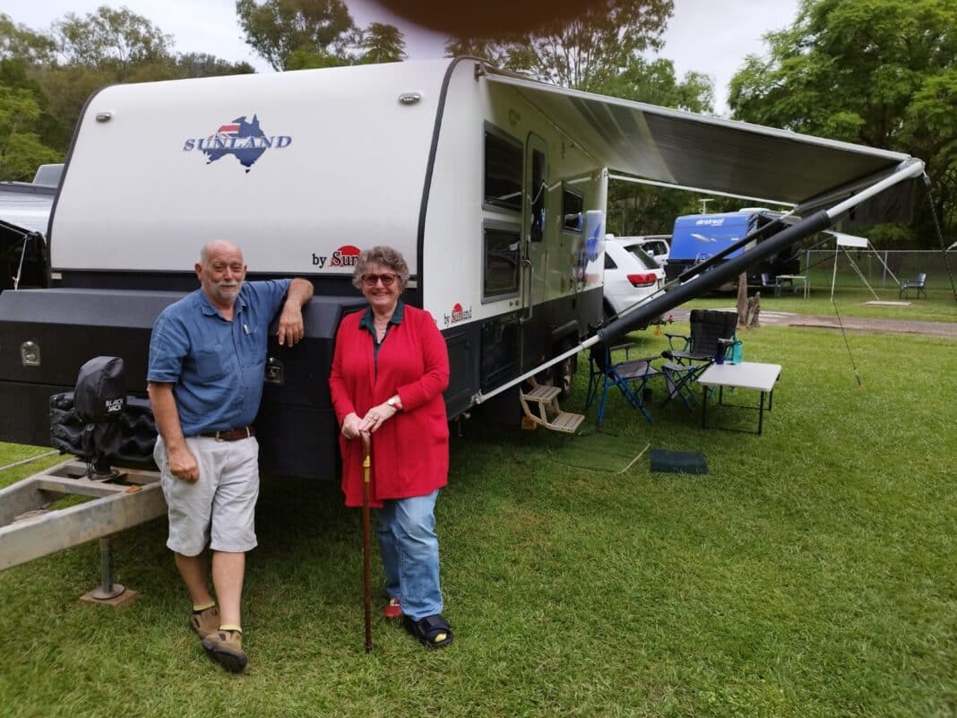 Caravanning journalist Alison Huth sporting a moon boot with husband Peter stand in front of their caravan at a campsite