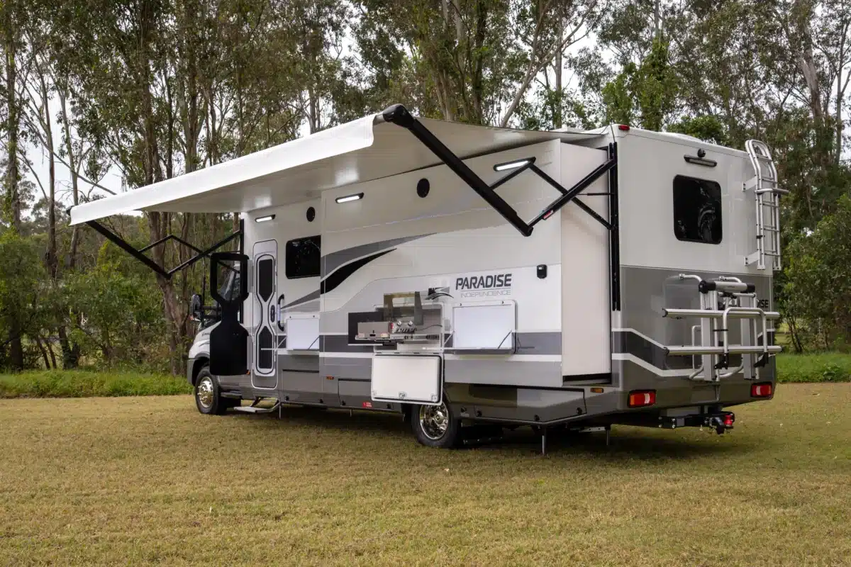 Rear three-quarter view of the Paradise Independence Platinum motorhome with awning and slide-out deployed
