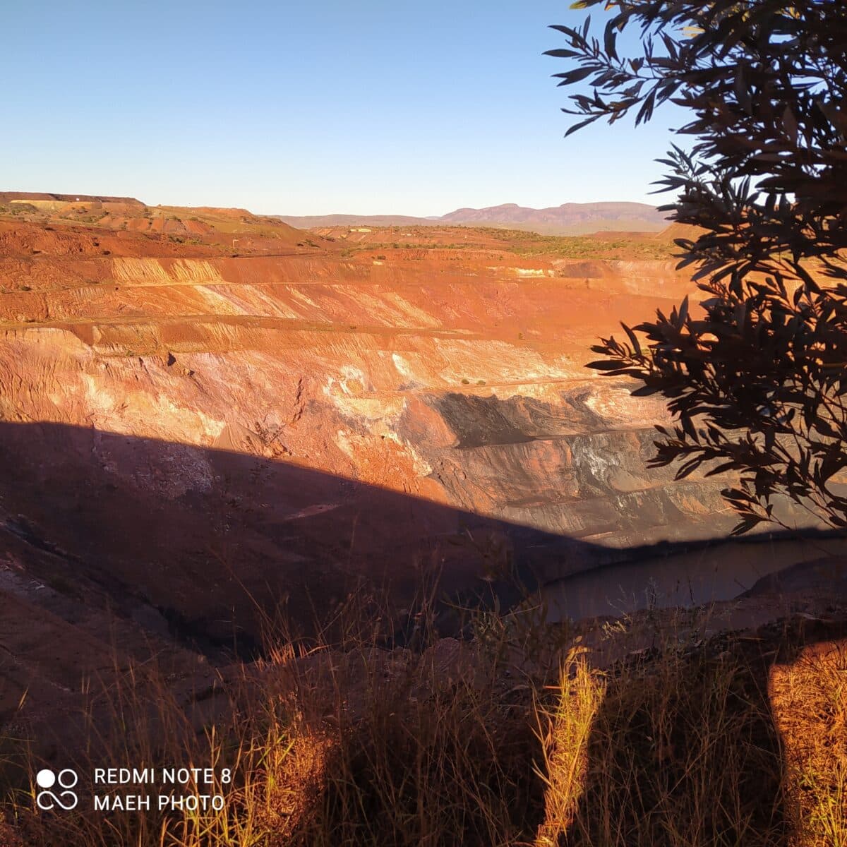 View from inside a tour bus looking out at a red dirt haul road and terraced mine cuts at Rio Tinto Tom Price Mine