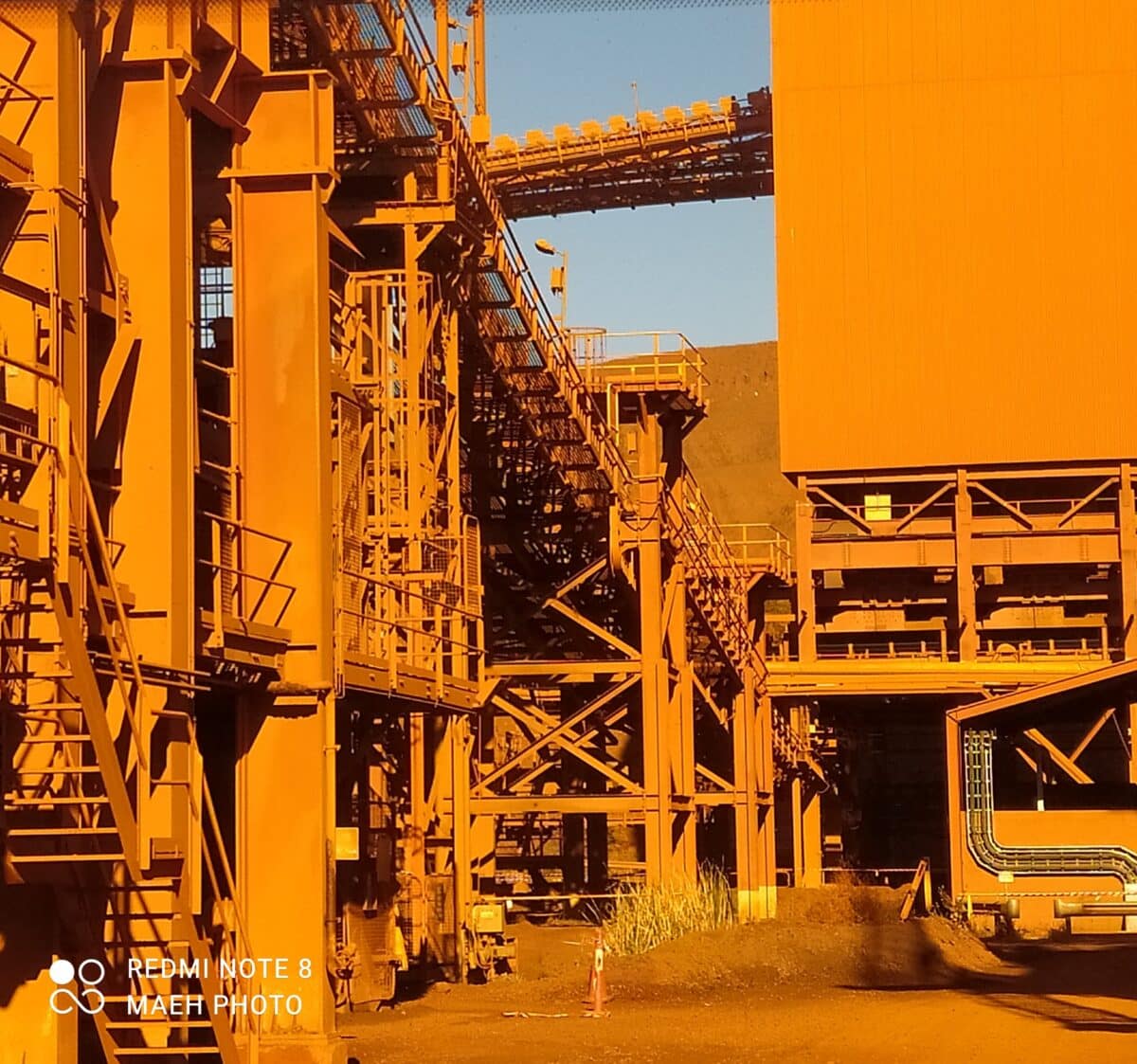 A group of tourists wearing hard hats inspecting a massive mining excavator at the Tom Price Mine viewing area