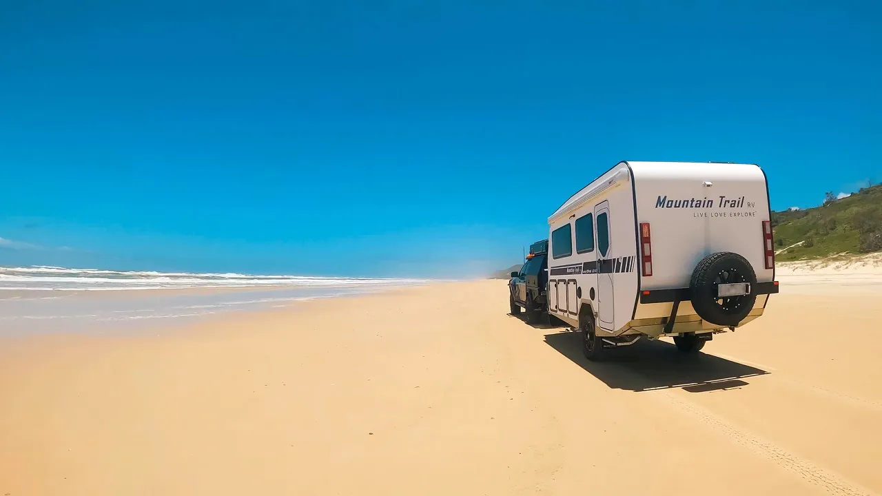 Caravan driving along a wide Australian beach under a clear blue sky