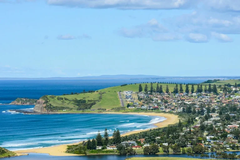 Aerial view of Kiama NSW showing Surf Beach, the lagoon, residential streets lined with Norfolk Island pines, rolling green headlands and the Tasman Sea beyond