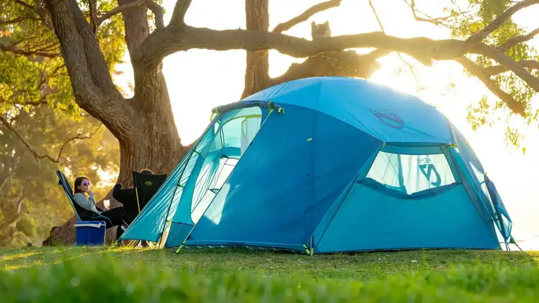Nemo-Aurora-Highrise-Camping-Tent-rating blue tent with sun backdrop under big tree lifestyle