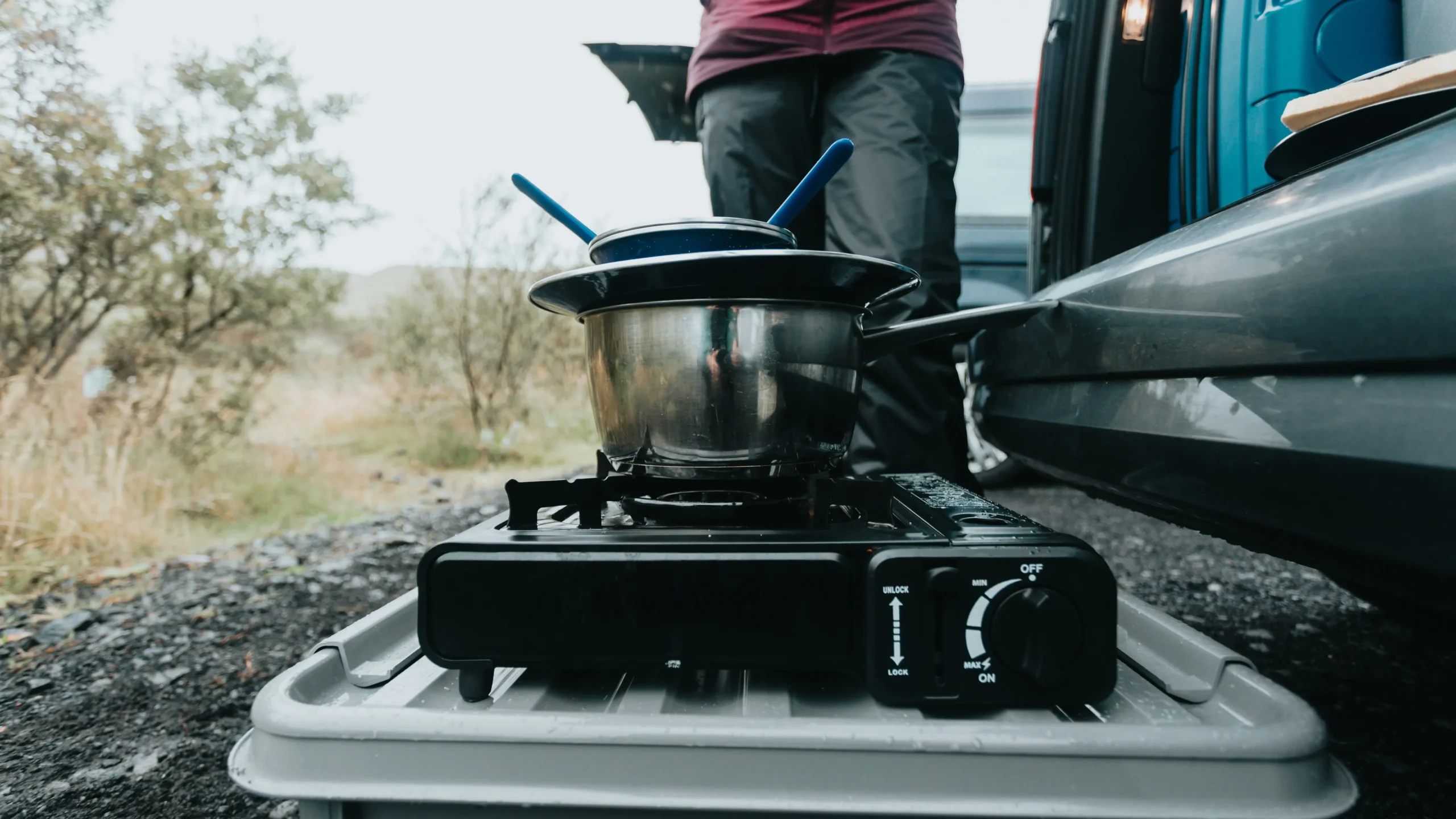 Portable butane gas stove sitting on box cooking out the back of a van