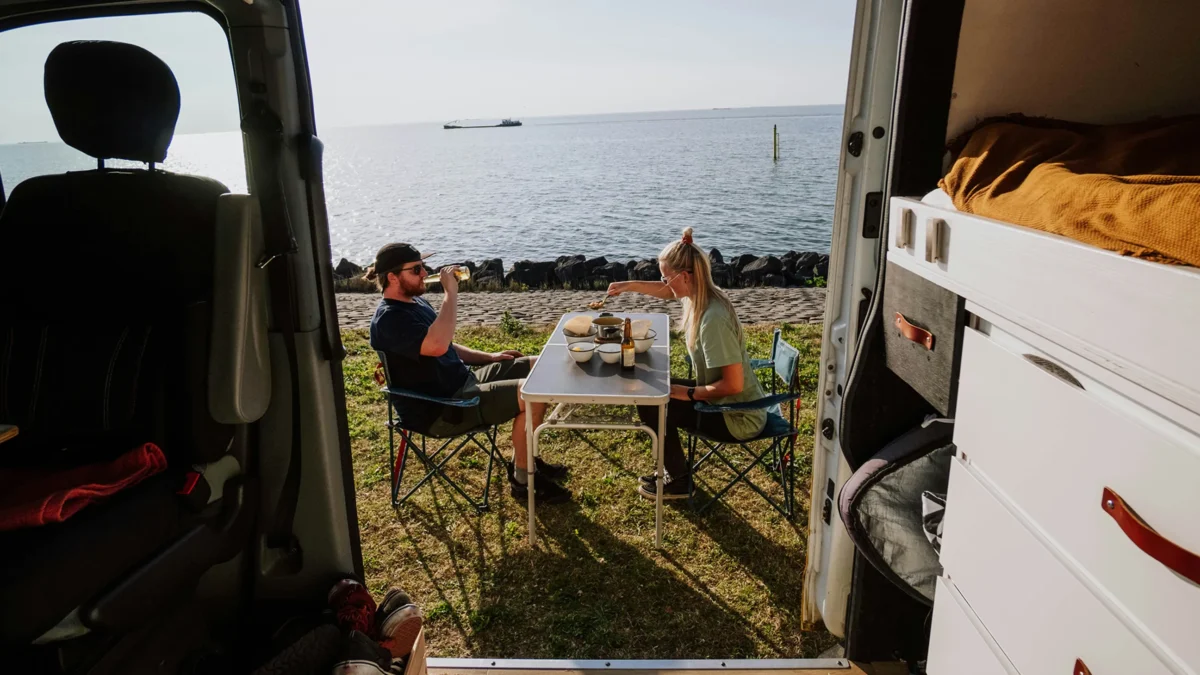 couple sitting by sea having lunch outside of camper