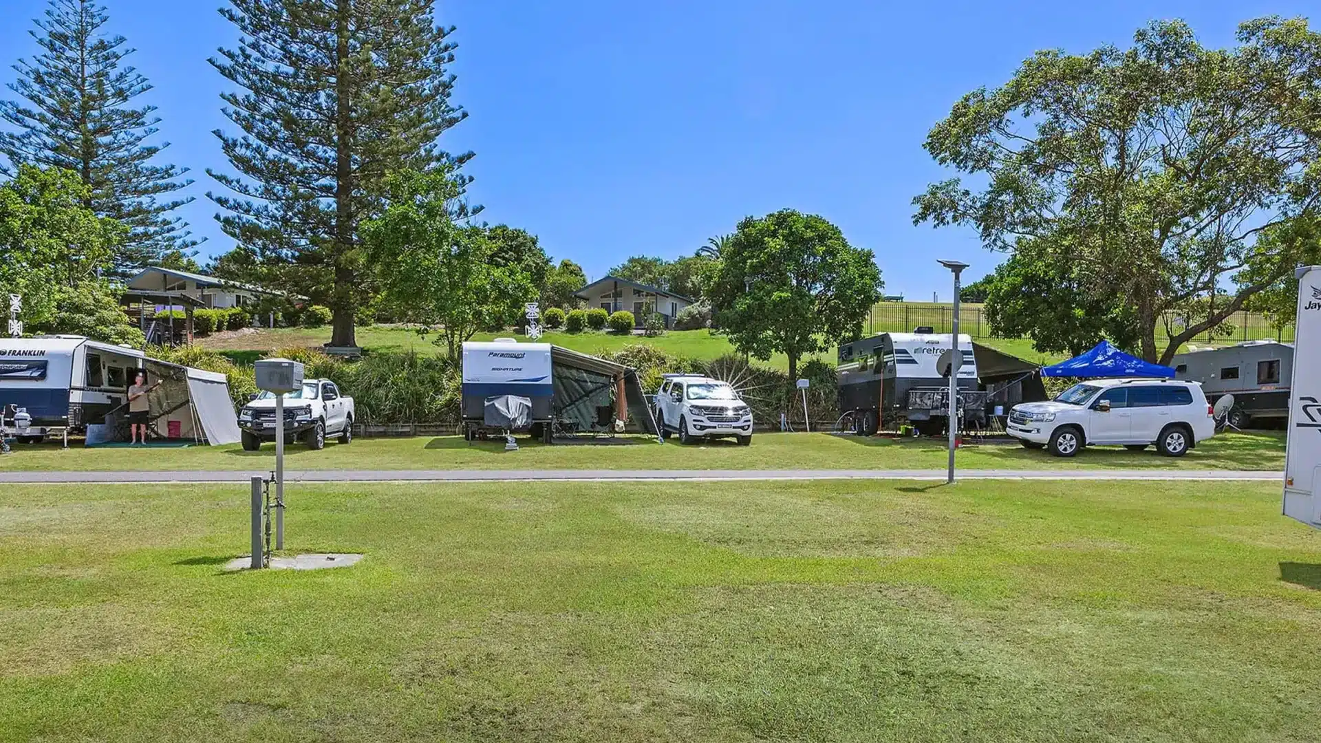 Caravans, camper trailers and four-wheel drives on grassy sites at a Queensland holiday park under tall pines