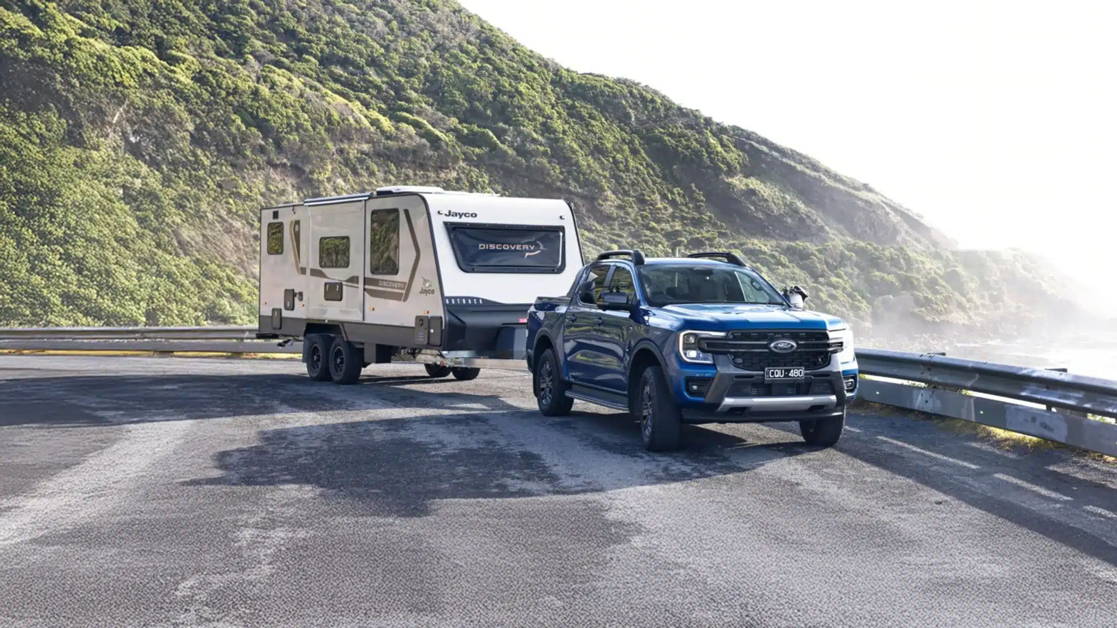 blue truck ute towing jayco caravan on coastal road
