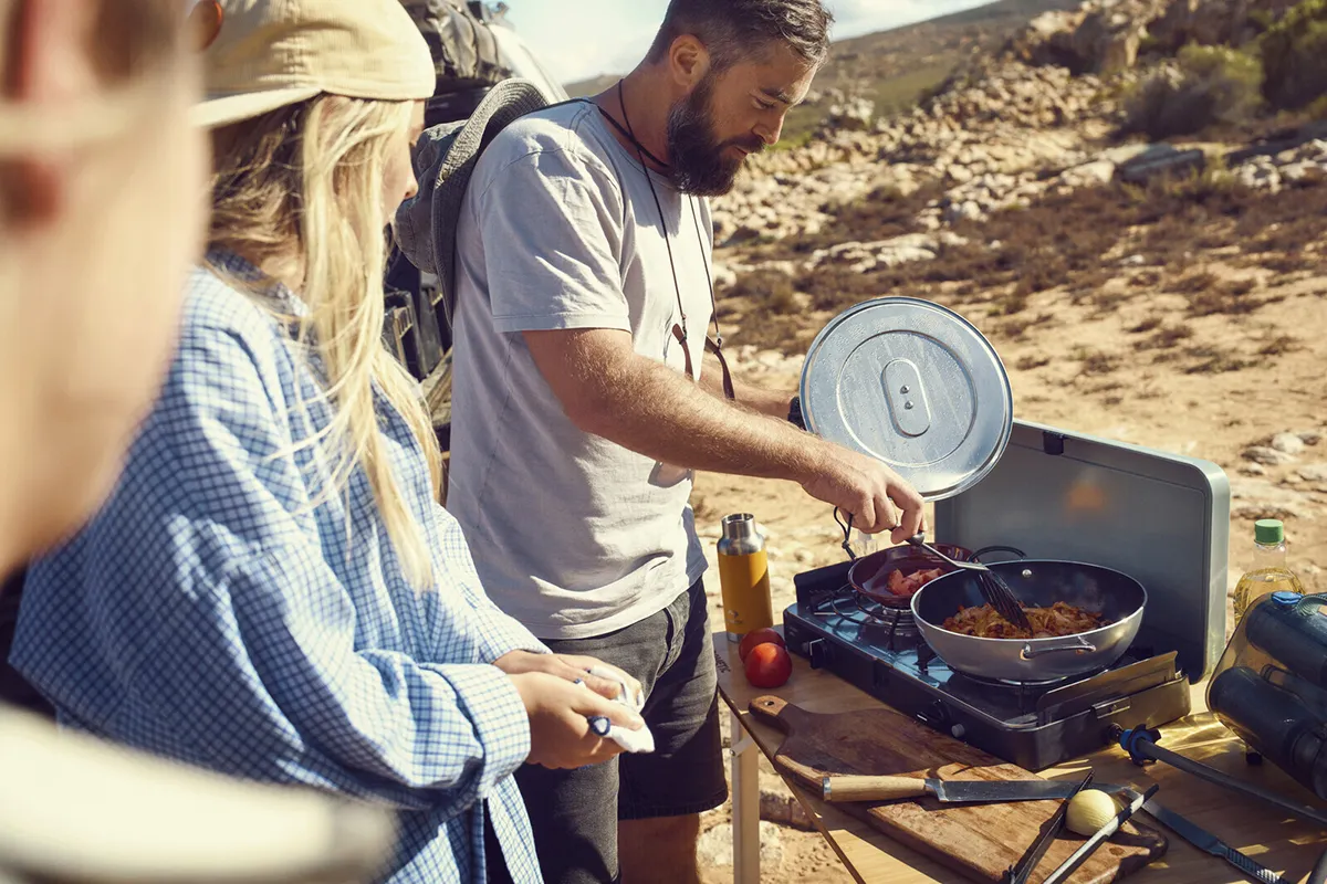 Family preparing an affordable meal on a portable stove while at camp site in a remote outdoor setting