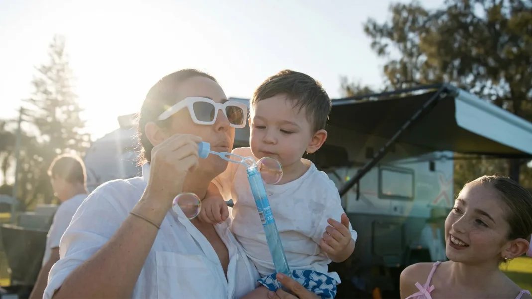 family-caravan-park-bubbles-holiday Family relaxing at a caravan park with children playing and blowing bubbles during a holiday affordable holidays