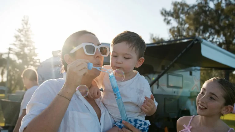 Family relaxing at a caravan park with children playing and blowing bubbles during a holiday affordable holidays