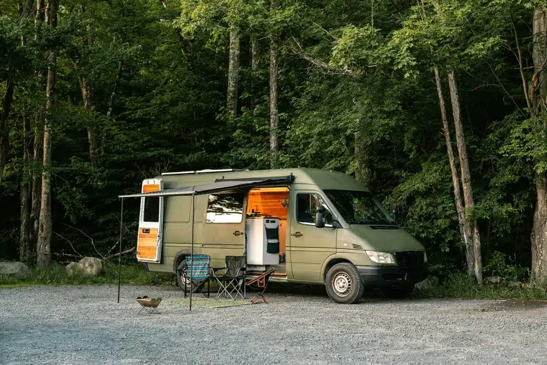 Campervan set up for off-grid camping in forest with outdoor seating and awning