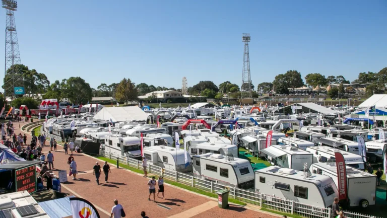 Aerial view of hundreds of caravans and motorhomes on display at an Australian caravan and camping show, with crowds of visitors walking the aisles between exhibitor stands
