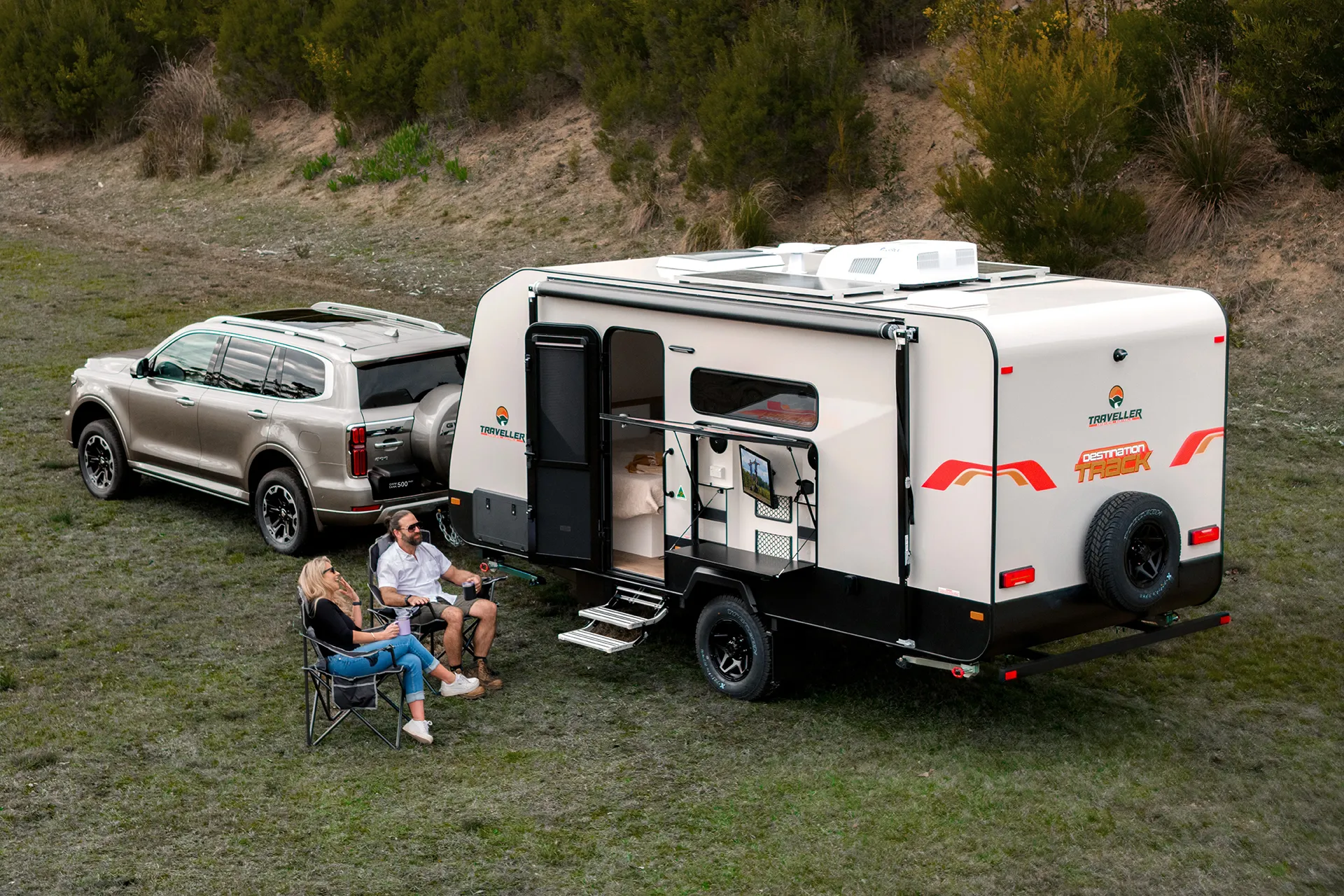 Traveller Caravans Destination Track caravan set up at a campsite with a couple relaxing beside their SUV tow vehicle.