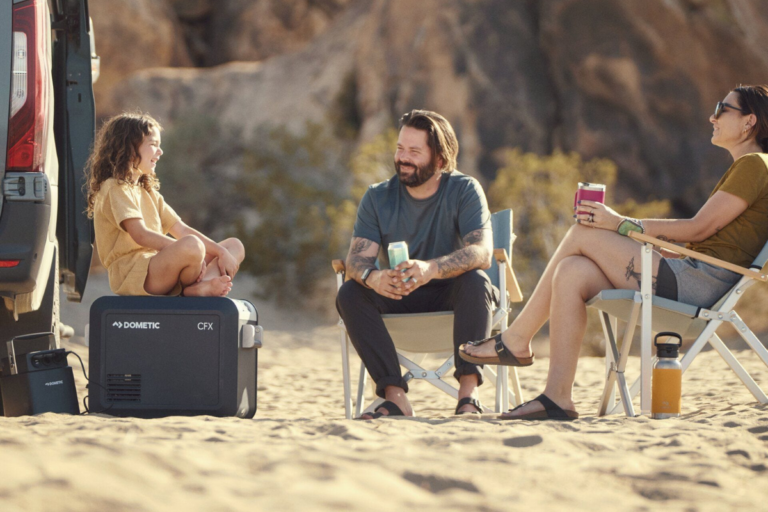 mum, dad and child on beach with dometic fridge and camp chairs with drinks