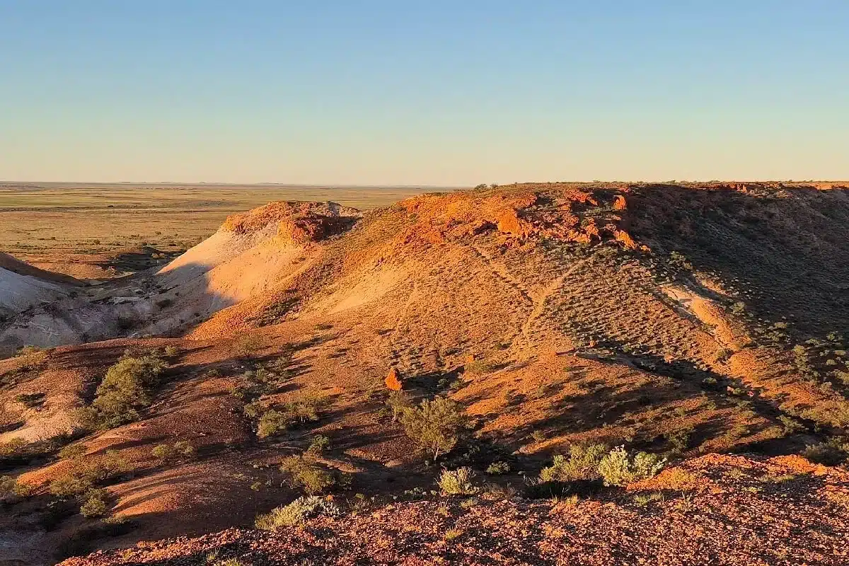 Golden hour view of rugged red rock escarpments and sweeping desert plains typical of an Australian outback touring route.