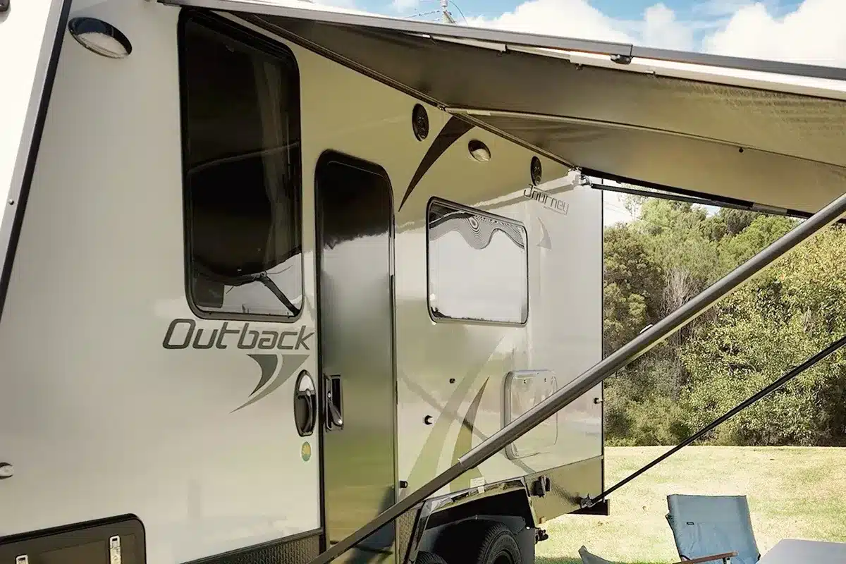Dometic anti-flap kit fitted to the side of a Jayco Journey Outback caravan with awning extended over a grassy campsite