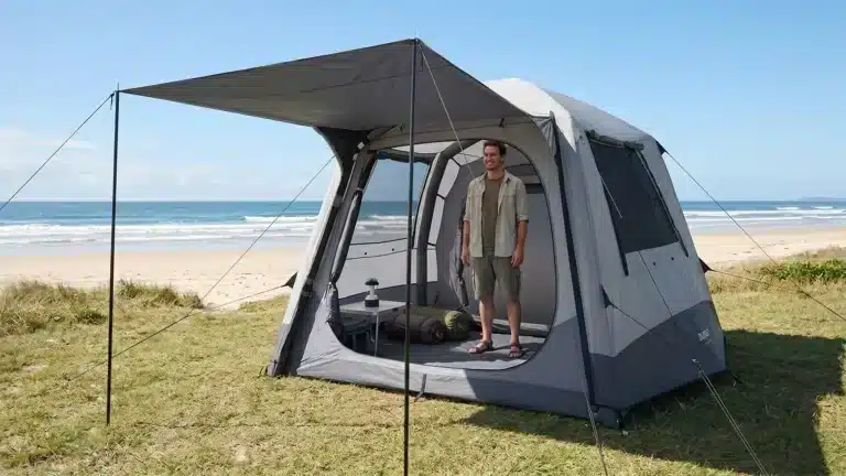 Man standing inside an open Dune 4WD Ultimate Air Tent on a grassy beachfront campsite, demonstrating the tent's full stand-up interior height