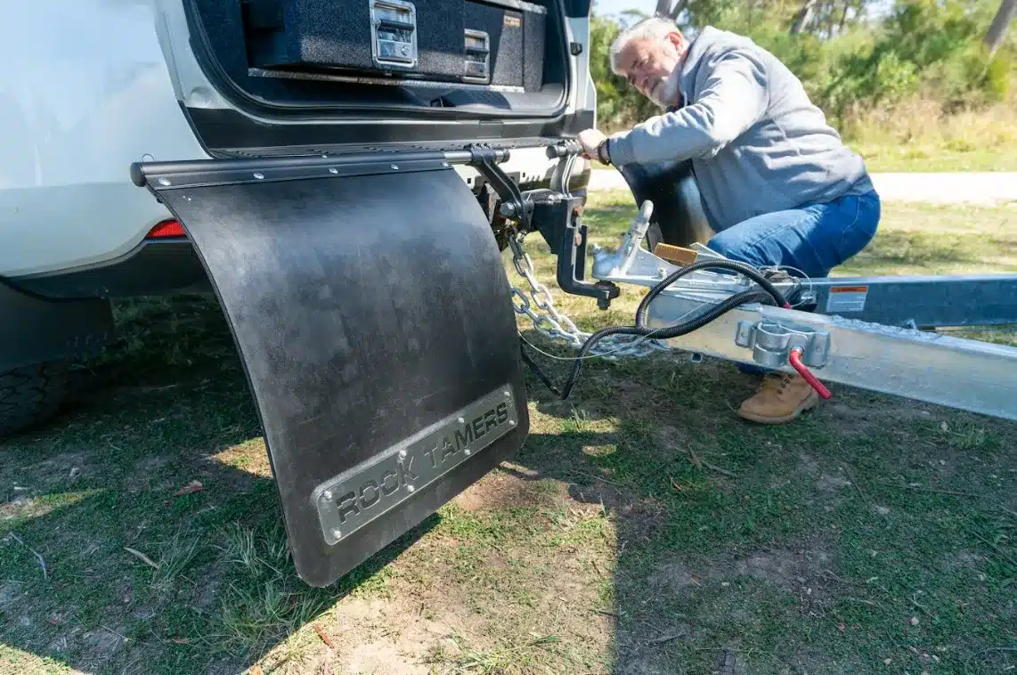 man tinkering with the rear of his car that has rock tamers mudguard installed on it