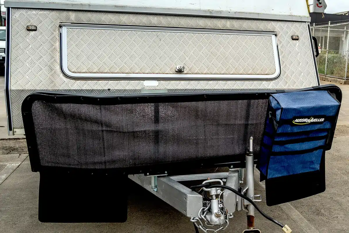 Aussie Traveller A-frame stone guard fitted to a pop-top caravan drawbar, showing black mesh panel, rubber mud flaps, and branded storage bag