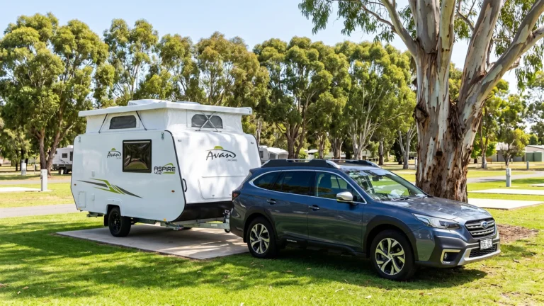 Avan Aspire 402 pop-top caravan hitched to a Subaru Outback at a shaded Australian holiday park, showing the compact single-axle van's raised pop-top roof and lightweight profile