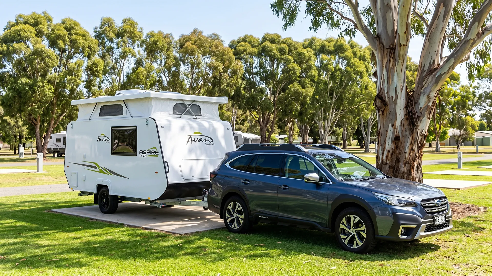 Avan Aspire 402 pop-top caravan hitched to a Subaru Outback at a shaded Australian holiday park, showing the compact single-axle van's raised pop-top roof and lightweight profile
