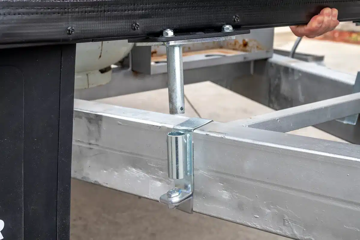 Close-up of a caravan stone guard U-bracket being fitted to a galvanised A-frame drawbar, showing the mounting hardware and mesh panel above