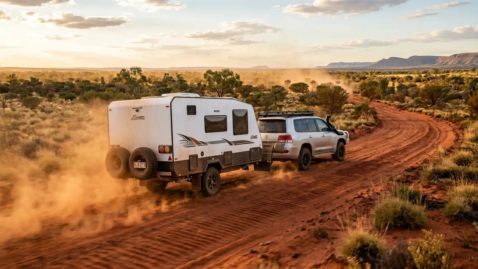 caravan-stone-guard-outback-red-dirt-road-hero A 4WD towing a white off-road caravan along a corrugated red dirt outback road, dust billowing from the rear tyres, illustrating why caravan stone protection is essential on Australian gravel roads