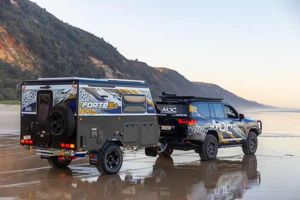 MDC Forte 9 Plus hybrid camper hitched to a black 4WD on a Queensland beach at dusk, illustrating off-road towing capability in an Australian coastal setting