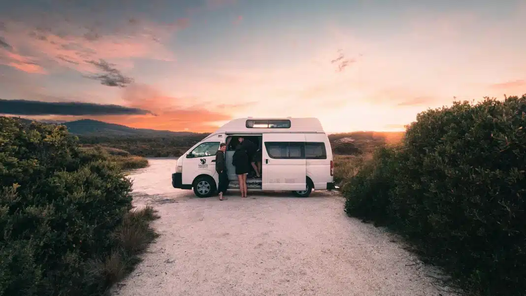 arriving at a remote Australian coastal campsite at sunset beside a white high-top campervan, with scrubland and mountain ranges in the background