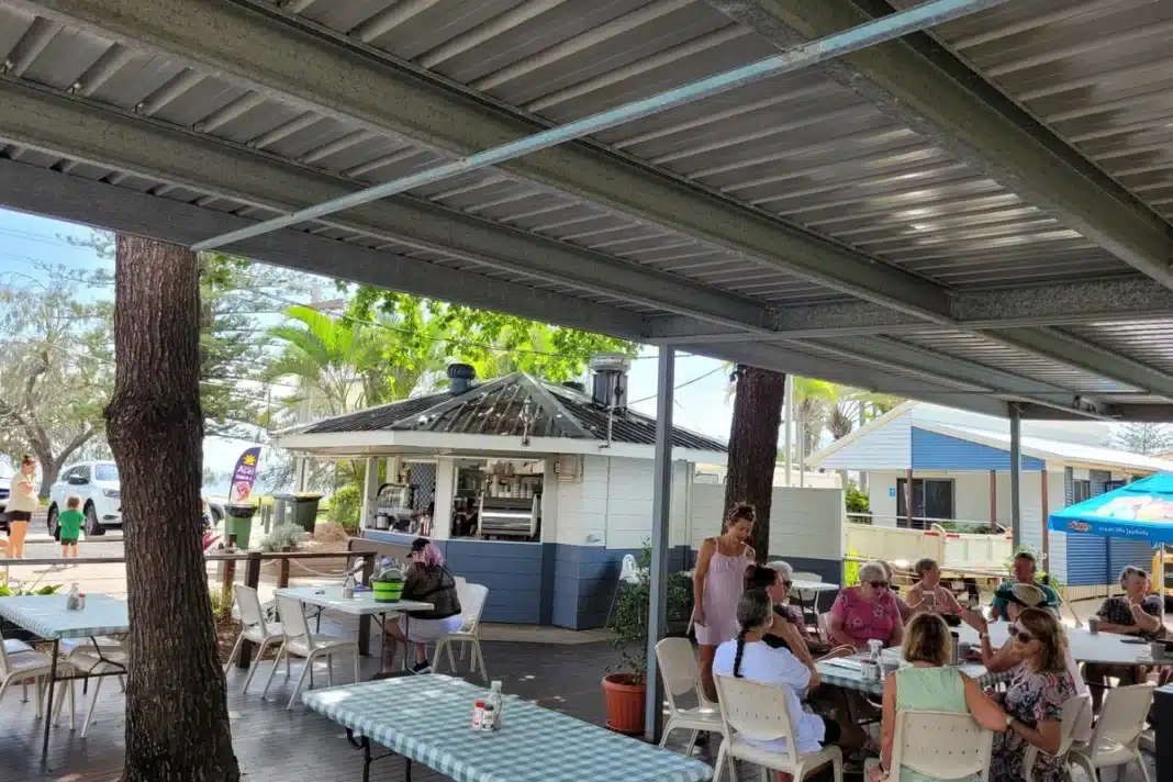 salty-seas-cafe-woodgate-beach-holiday-park Guests dining at Salty Seas Cafe at NRMA Woodgate Beach Holiday Park with the outdoor covered deck area and cafe kiosk visible