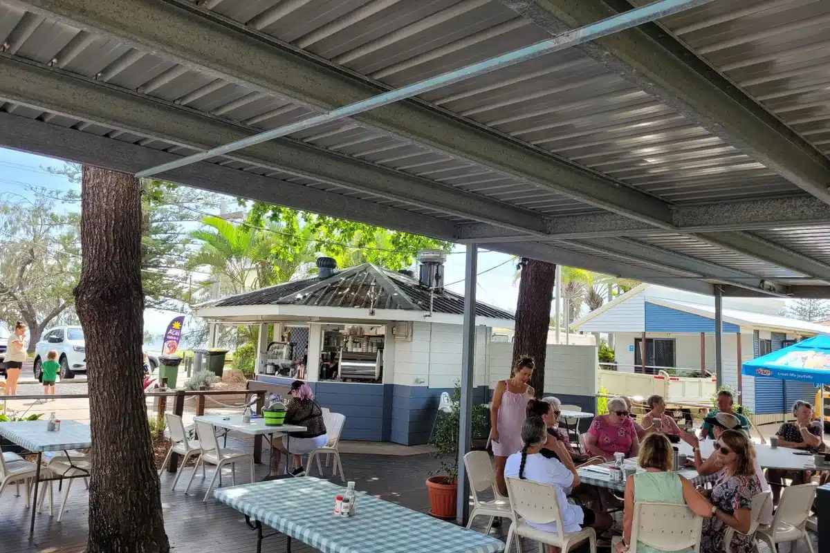 Guests dining at Salty Seas Cafe at NRMA Woodgate Beach Holiday Park with the outdoor covered deck area and cafe kiosk visible