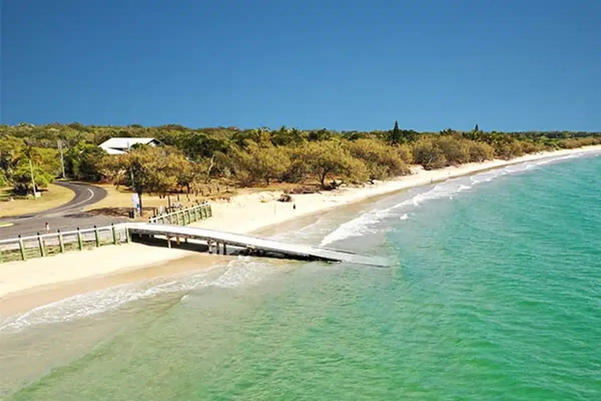 Concrete boat ramp at Woodgate Beach with turquoise water and the long sandy shoreline stretching into the distance under a clear blue sky