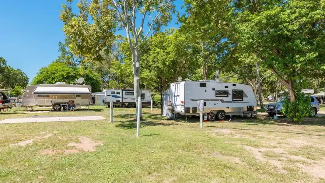woodgate-beach-caravans-under-trees Powered caravan sites at NRMA Woodgate Beach Holiday Park with multiple vans parked under mature trees on a sunny day