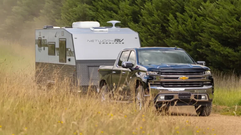 Network RV Caravans branded off-road caravan towed by a black Chevrolet Silverado along a country dirt track
