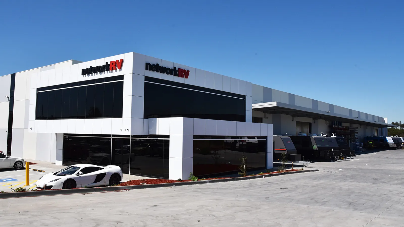 Network RV branded dealership showroom exterior with caravans lined up alongside the building