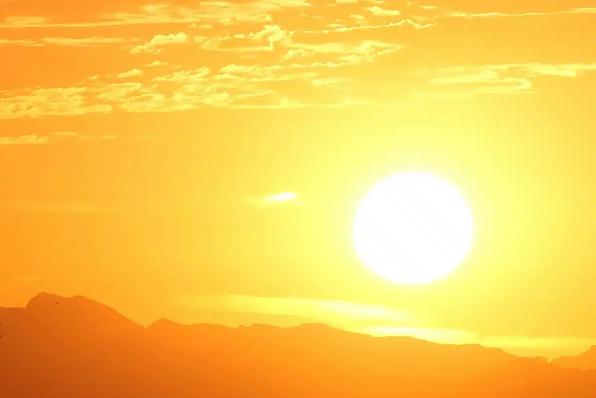 Intense Australian outback sunset with a large white sun over dark mountain silhouettes in a deep orange sky