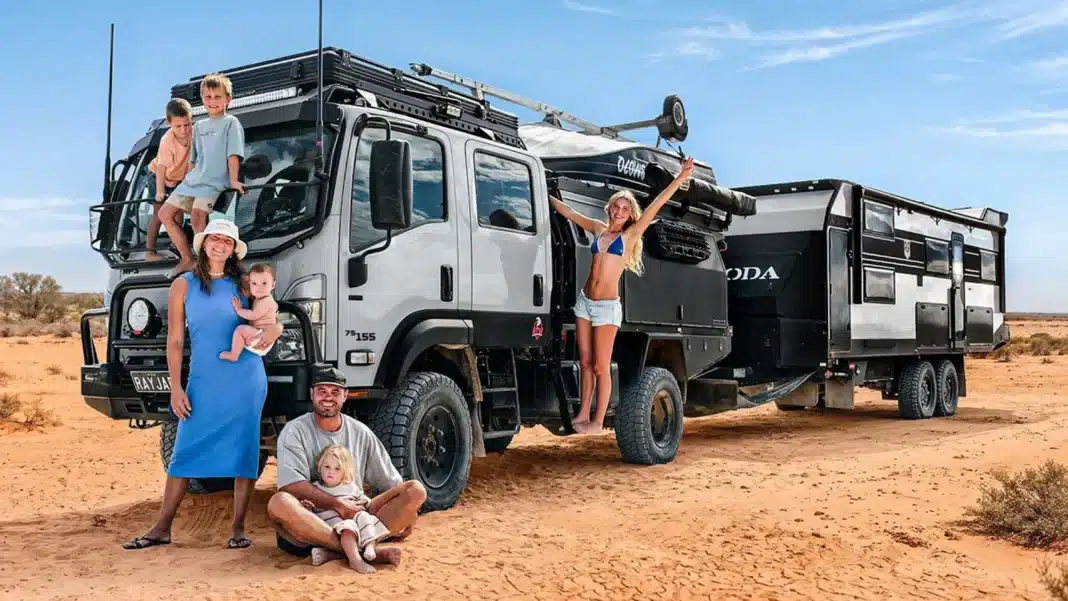 cartwrights-kokoda-caravans A young Australian family of five poses with their massive, premium 4x4 Isuzu expedition truck and large fifth-wheeler caravan in a remote red desert landscape.