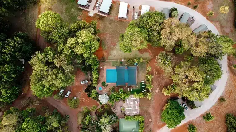 Aerial view of Discovery Parks Breeze in Katherine, NT, showcasing the central swimming pool surrounded by shady trees and holiday park cabins.