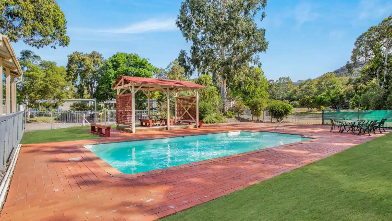 Brick-paved outdoor swimming pool and shaded wooden seating area at Discovery Parks Grampians, set among native Australian trees.