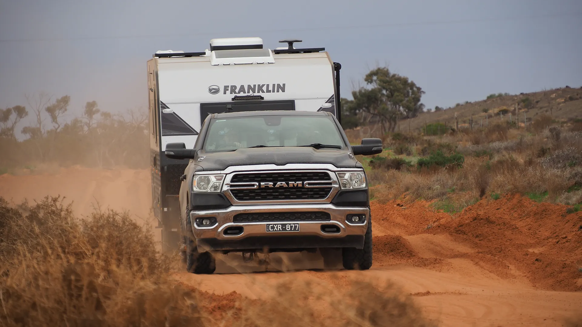 off-road-caravanning RAM ute and Franklin caravan raising a thick dust trail on a red dirt outback road