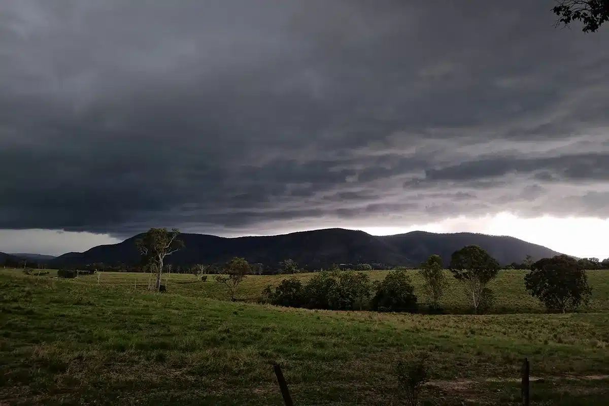 Dark storm clouds building over green farmland and hills in regional Australia ahead of a severe thunderstorm warning