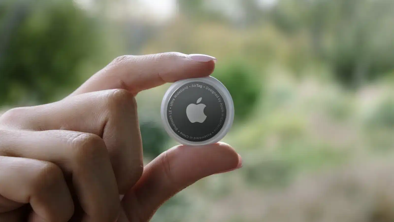 Hand holding an Apple AirTag showing the Bluetooth LE and Ultra Wideband markings around the edge