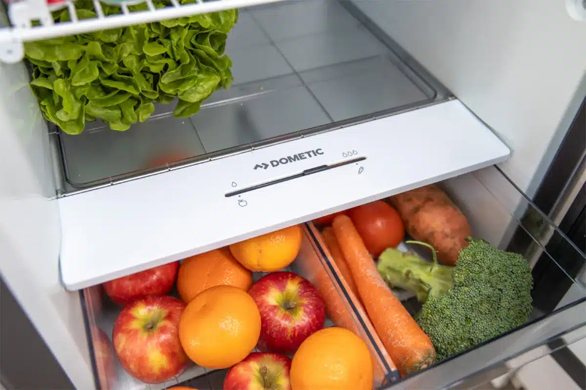 Open Dometic caravan fridge crisper drawer stocked with fresh fruit and vegetables