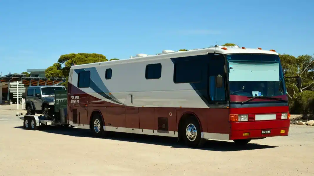 Converted maroon and silver coach towing a four-wheel drive on a car trailer, parked at Eucla on the Nullarbor
