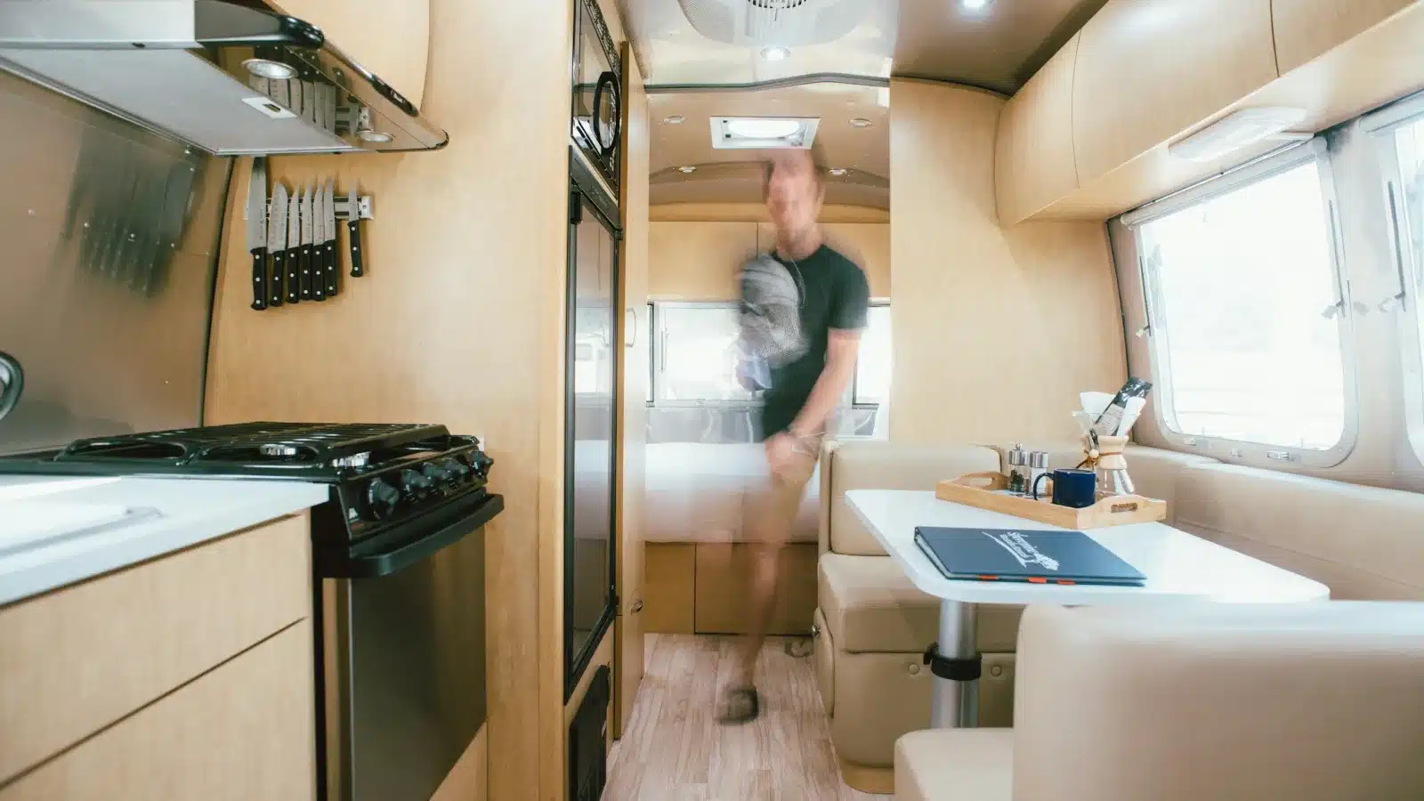 Caravan kitchen with a gas cooktop, knife rack and curved overhead cupboards, with a dinette behind