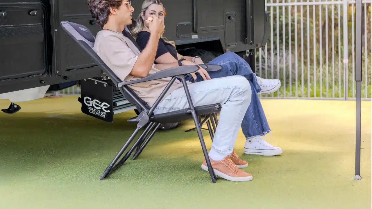Couple relaxing in camp chairs beside a Gold Class AC17C off-road caravan